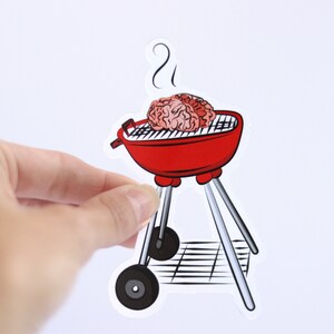 May include: A red and black grill with two brains on the grill grate. There is steam coming from the grill.