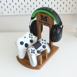 May include: A wooden stand with a personalized nameplate that holds two video game controllers and a pair of green and black headphones. The nameplate reads "M Michael Madlines".