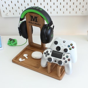 Könnte beinhalten: Eine Holz-Gaming-Station mit einem schwarzen und grünen Headset, zwei weißen Gamecontrollern und einer Ladestation für Ohrhörer. Auf der Station sind der Buchstabe "M" und der Name "Michael Martinez" eingraviert. Für Gamer.