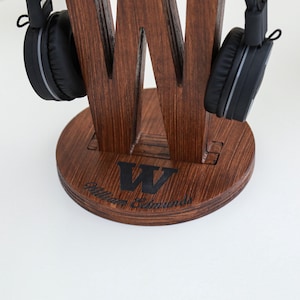 May include: A wooden headphone stand in a dark brown finish, shaped like a large letter "W". The stand has a circular base with the name "William Edmunds" and a "W" logo. Black headphones hang on the stand.