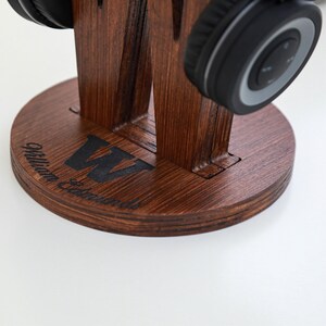 May include: A wooden headphone stand with a dark brown finish. The stand features a circular base with the name "William Edmunds" and a large "W" etched into the wood. Black headphones rest on the stand.