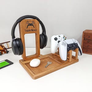 Pode incluir: Estação de jogos de madeira com suporte para fones de ouvido, suportes para controladores e uma bandeja para acessórios. Inclui um fone de ouvido preto, dois controladores brancos, um mouse branco e uma chave. O suporte tem o texto "SuperNova".