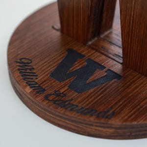 May include: A dark brown wooden beer flight with a circular base. The base features the name "William Edmunds" and a large black "W" logo. The wood grain is visible, and the design is set against a white background.