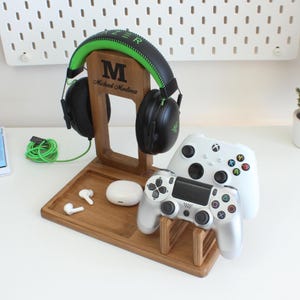 May include: A wooden gaming console stand with a headset holder, two controller slots, and a small compartment for earbuds. The stand is personalized with the name "Michael Martinez".