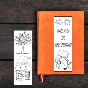 May include: Black and white printable bookmark featuring a fox with a pumpkin, a tree with leaves, and a dog with a book. The bookmark has the text "BOOKS IN AUTUMN" and two fall leaves.