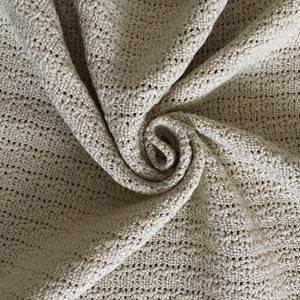 Peut inclure: Un gros plan d'une couverture en tricot beige avec un motif texturé. La couverture est pliée et tordue en forme de spirale.