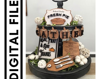 May include: A tiered tray decorated for Thanksgiving with a "Gather" banner, a "Eat, Pray & Give Thanks" sign, a "Baked Daily Fresh Pie" sign, a Thanksgiving menu sign, and a wooden tag with a fork and spoon design.