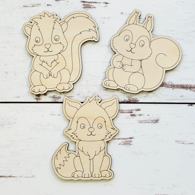 May include: Three unfinished wooden cutouts of woodland animals: a squirrel, a fox, and a skunk. The animals are all in a sitting position with their tails curled behind them.