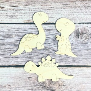 May include: Three unfinished wooden dinosaur shapes, ready to be painted. The dinosaurs are a stegosaurus, a brachiosaurus, and a tyrannosaurus rex.