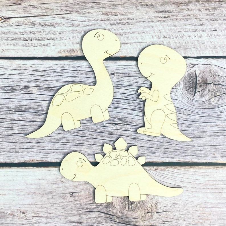 May include: Three unfinished wooden dinosaur shapes, ready to be painted. The dinosaurs are a stegosaurus, a brachiosaurus, and a tyrannosaurus rex.