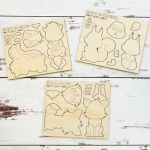 May include: Three wooden craft kits for building a skunk, a fox, and a squirrel. Each kit includes multiple pieces that can be painted and glued together. The kits are labeled "Build-a-Skunk", "Build-a-Fox", and "Build-a-Squirrel".