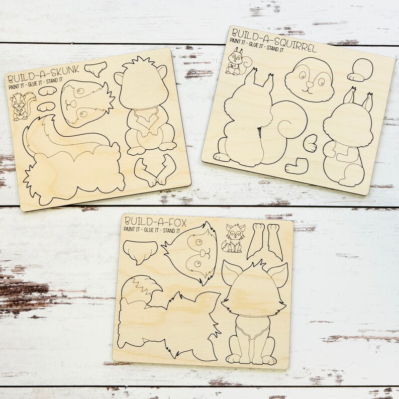 May include: Three wooden craft kits for building a skunk, a fox, and a squirrel. Each kit includes multiple pieces that can be painted and glued together. The kits are labeled "Build-a-Skunk", "Build-a-Fox", and "Build-a-Squirrel".