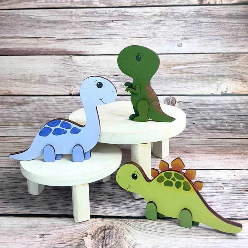 May include: Three wooden dinosaur figurines on small wooden stands. The dinosaurs are blue, green, and green with orange accents. The stands are painted white.