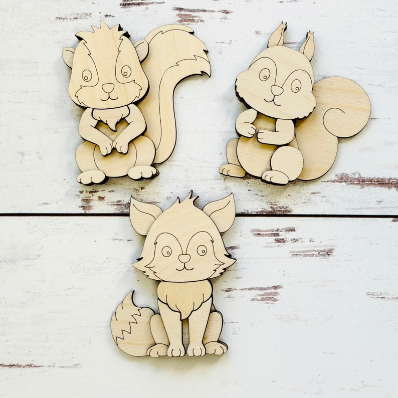 May include: Three unfinished wooden animal cutouts: a squirrel, a fox, and another squirrel. The cutouts are ready to be painted or decorated.