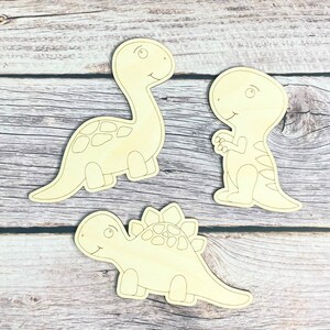 May include: Three unfinished wooden dinosaur shapes, ready to be painted. The dinosaurs are a brachiosaurus, a stegosaurus, and a tyrannosaurus rex.