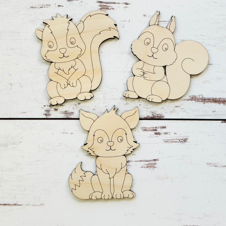 May include: Three unfinished wooden cutouts of woodland animals: a squirrel, a fox, and a skunk. The animals are all sitting with their tails curled behind them.
