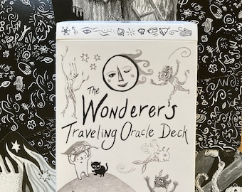 May include: A white box with black illustrations of whimsical creatures and a moon with a winking eye. The box reads "The Wanderer's Traveling Oracle Deck" and "36 cards illustrated by Marika McCool."