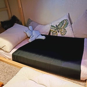 Puede incluir: Un edred&oacute;n con estampado blanco y negro con una almohada blanca y un animal de peluche azul en la parte superior. La cama est&aacute; contra una pared con una almohada blanca con forma de mariposa y una almohada blanca texturizada.