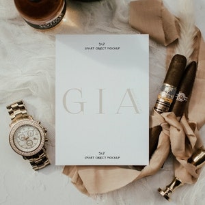 May include: A white card with the text "GIA" in a light grey font. The card is on a white surface with a brown ribbon, two cigars, a gold watch, and two bottles of alcohol.