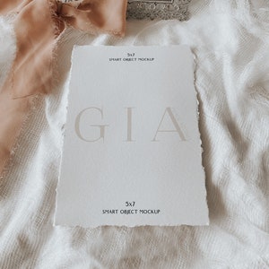 May include: A white card with the text "GIA" in a light grey font. The card is on a white fabric background with a silver frame and a peach-coloured ribbon.