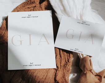 以下が含まれることがあります： 白いカード2枚に黒い文字で「GIA」と「SMART OBJECT MOCKUP」と書かれている。カードは、白いパンパスグラスの束が置かれた茶色の布地に置かれている。