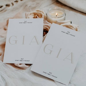 May include: Two white cards with the text "GIA" in a serif font. The cards are on a white fabric background with a lit candle and flowers.