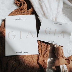 Op de afbeelding: Twee witte kaarten met de tekst "GIA" en "SMART OBJECT MOCKUP" in zwarte tekst. De kaarten liggen op een bruine stoffen ondergrond met een boeket witte pampasgras.