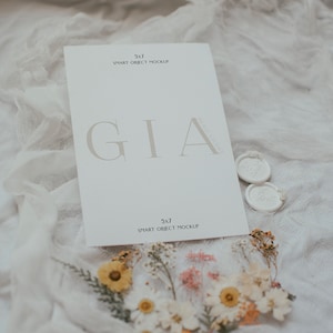 May include: A white card with the text "GIA" in a serif font. The card is on a white fabric background with dried flowers and wax seals.