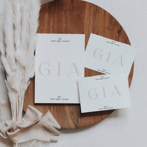 May include: A stationery mockup with white cards printed with the word "GIA" in a soft font. The cards are displayed on a wooden tray, with a lit candle and dried flowers. The text "5x7 SMART OBJECT MOCKUP" and "3x5 SMART OBJECT MOCKUP" is also visible.