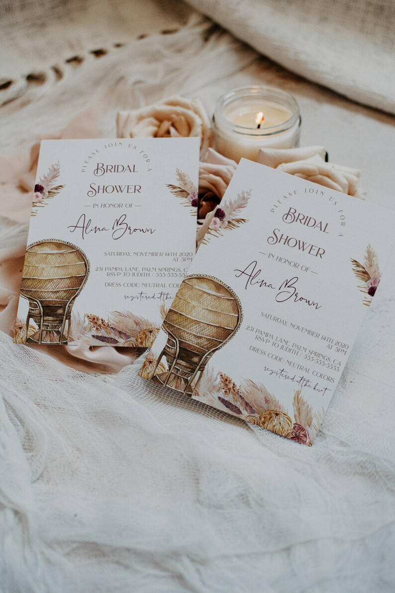May include: Two white cards with a boho floral design and a wicker chair illustration. The text on the cards reads "Please join us for a bridal shower in honor of Alina Brown" and includes the date, time, and location of the event.