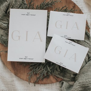 Peut inclure: Trois cartes blanches avec le texte "GIA" en police de caract&egrave;res marron clair. Les cartes sont sur une surface en bois avec de la verdure et un tissu marron clair. Les cartes sont de tailles diff&eacute;rentes et portent le texte "SMART OBJECT MOCKUP" ainsi que les dimensions des cartes imprim&eacute;es dessus.