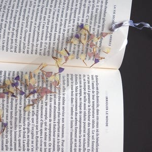 Peut inclure: Un livre avec un marque-page de fleurs pressées. Le marque-page est en résine transparente et présente des fleurs violettes et jaunes.