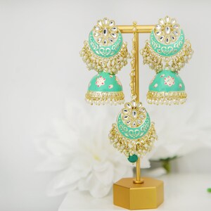 May include: A pair of green and gold earrings with pearl accents. The earrings are on a gold stand.