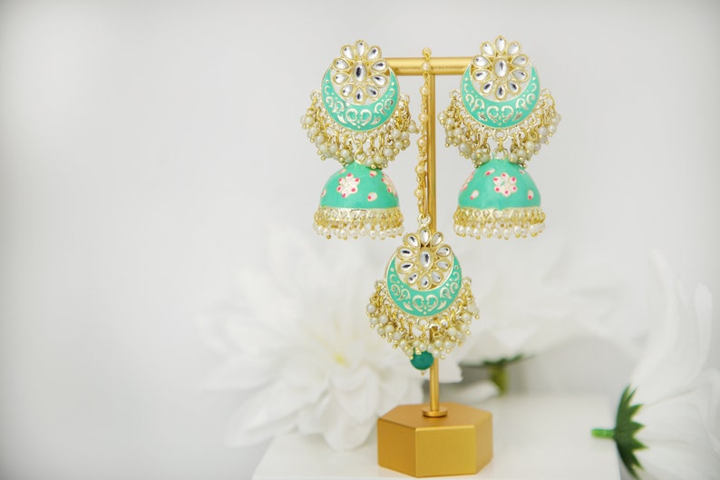 May include: A pair of green and gold earrings with pearl accents. The earrings are on a gold stand.
