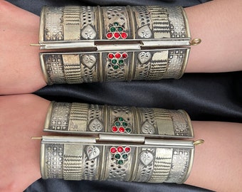 May include: A pair of silver hinged bracelets with intricate designs and red and green gemstones.