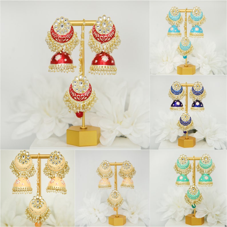 May include: A set of six pairs of traditional Indian earrings, each with a different color scheme. The earrings are made of gold metal and feature intricate designs with pearls and gemstones. The earrings are displayed on a gold stand.
