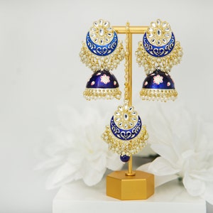 May include: A pair of blue and gold earrings with pearl accents. The earrings are on a gold stand. The earrings are a traditional Indian style.