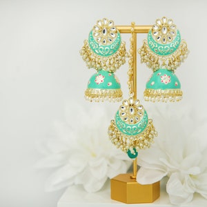 May include: A pair of teal blue Indian earrings with gold accents and pearl embellishments. The earrings are displayed on a gold stand.
