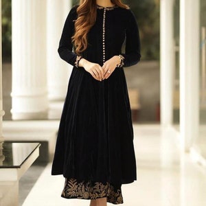 May include: A long, black velvet dress with long sleeves and a button-down front. The dress features gold embroidery on the cuffs and hem. The model is wearing gold earrings and nude heels.
