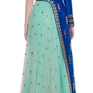 May include: A formal gown featuring a turquoise skirt adorned with gold embellishments. The bodice has a sheer back with gold detailing, and a single long blue sleeve with gold trim. The dress is suitable for special occasions.