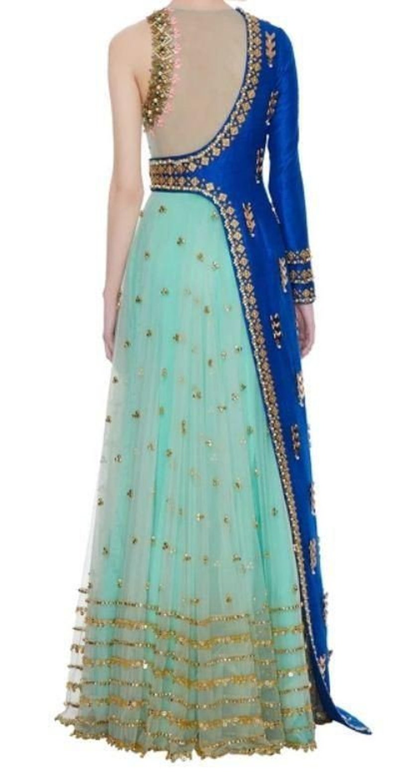 May include: A formal gown featuring a turquoise skirt adorned with gold embellishments. The bodice has a sheer back with gold detailing, and a single long blue sleeve with gold trim. The dress is suitable for special occasions.