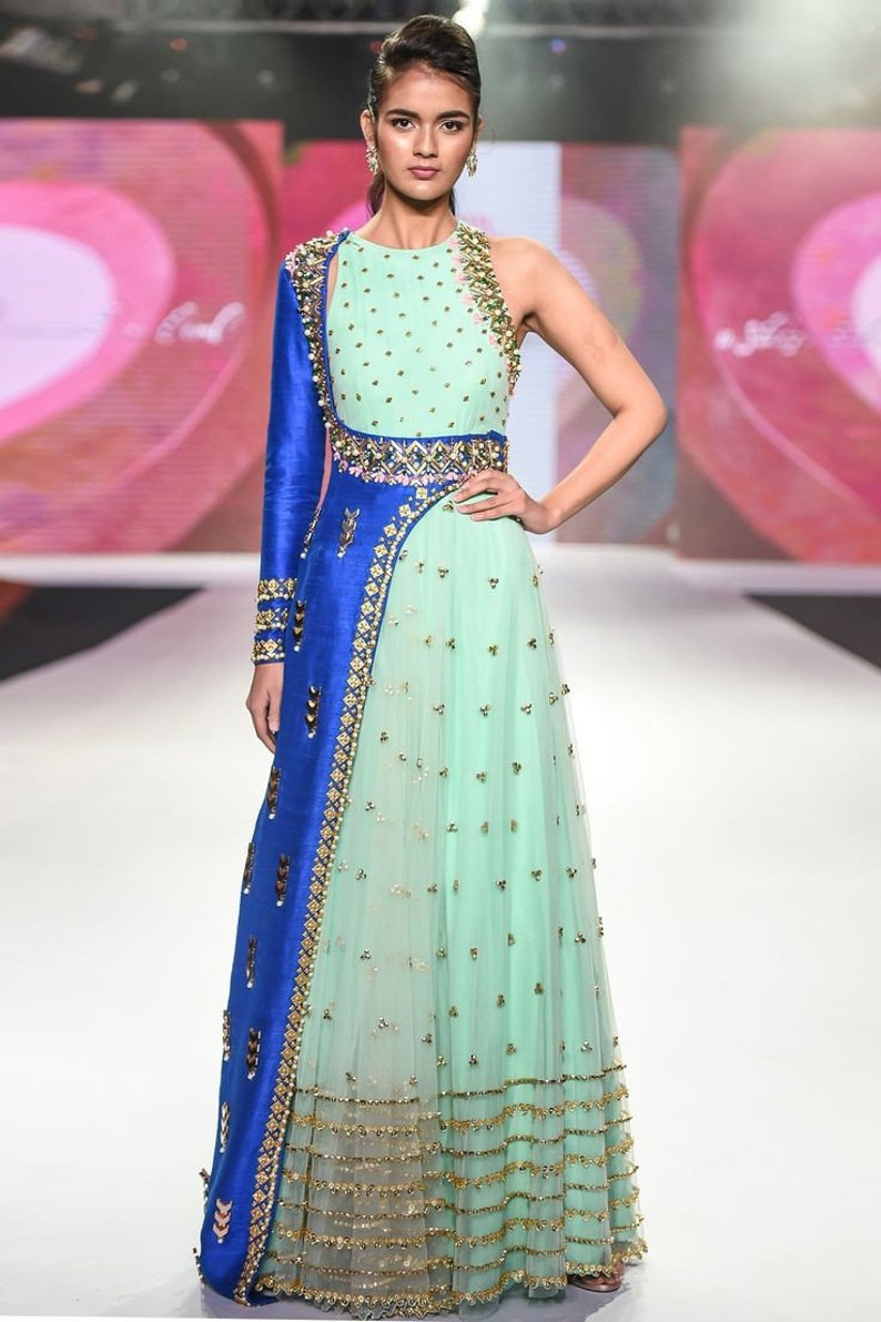 May include: A mint green and blue formal gown with gold embellishments. The dress features a one-shoulder design with a long blue sleeve and intricate gold detailing. The skirt is a flowing, layered design with gold accents.