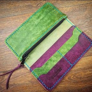 May include: A green and purple leather wallet with a zipped pocket and multiple card slots. The wallet has blue stitching and the text "Genuine Leather" is embossed on the front.