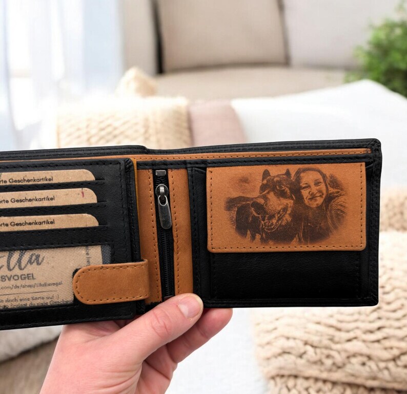 May include: A black leather wallet with a brown leather flap and a zippered pocket. The wallet has a personalized photo of a person and a dog engraved on the inside.