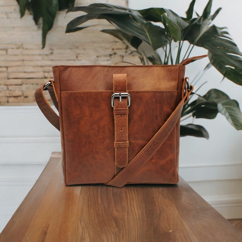 May include: A brown leather crossbody bag with a silver buckle and adjustable strap.