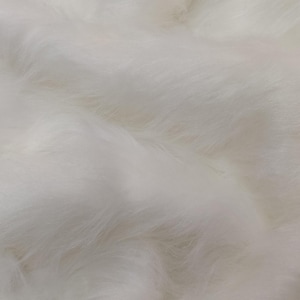 May include: White faux fur fabric with a soft, fluffy texture. The fur is arranged in a wavy pattern, creating a luxurious and cosy look.