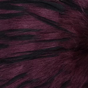 Peut inclure: Gros plan sur un tissu en fausse fourrure de couleur violet foncé et noir. Le tissu a une texture douce et moelleuse et un motif rayé.