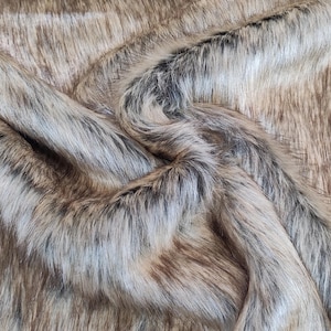 May include: A length of faux fur fabric featuring a blend of long, straight fibres in shades of light brown, tan, and dark charcoal grey. The material has a dense, shaggy texture with natural-looking colour variations throughout the surface.