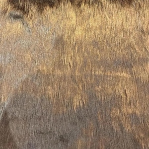 Könnte beinhalten: Nahaufnahme eines braunen und goldenen Kunstpelzes. Das Fell ist weich und flauschig mit einem dezenten Glanz.
