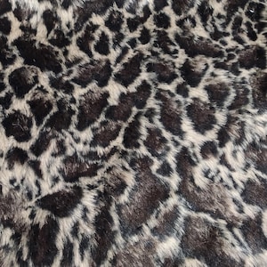 May include: Close-up of a leopard print faux fur fabric. The fabric has a pattern of dark brown and black spots on a beige background. The texture is soft and plush, with visible fibres. Ideal for clothing or home decor.
